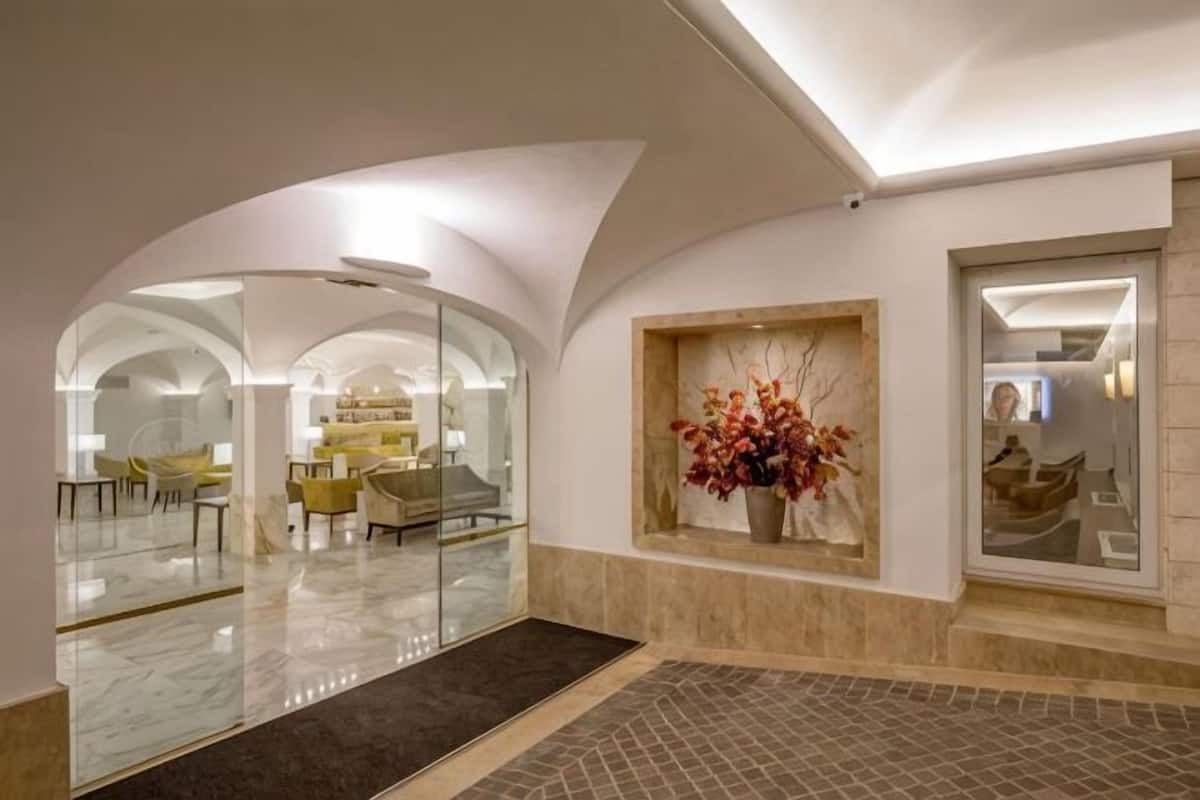Un interior con techos abovedados, un separador de vidrio, una zona de estar y un jarrón decorativo.