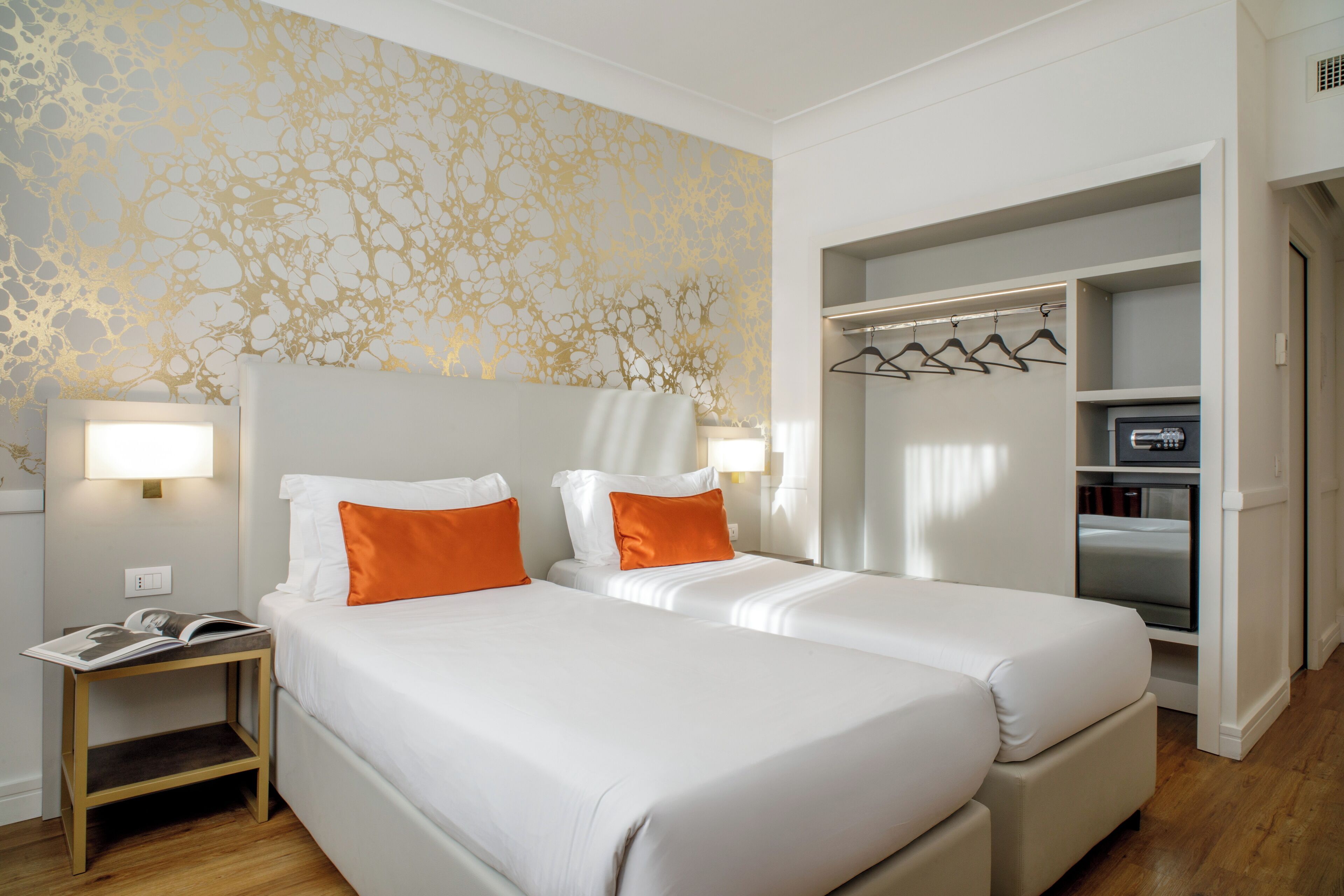 Une chambre d’hôtel avec deux lits, une table de chevet, un dressing et un mur orné d’un motif doré.