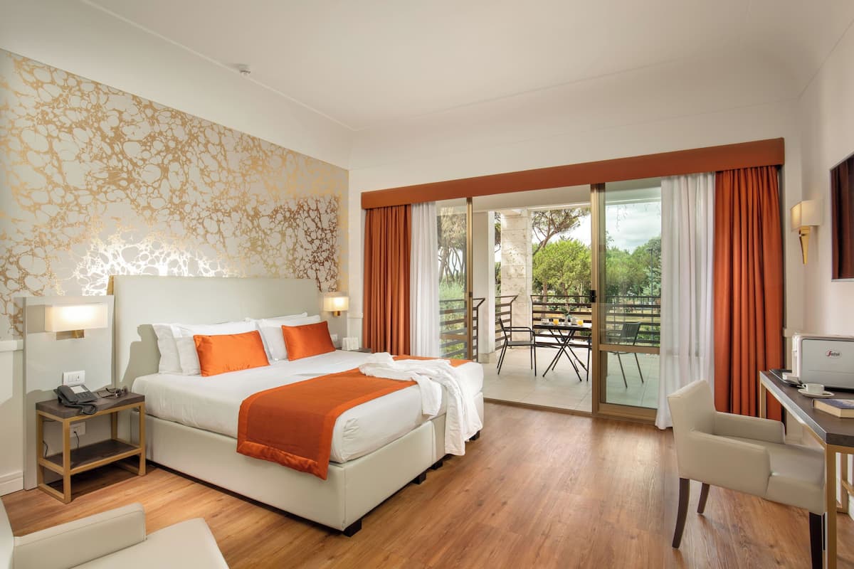 Una habitación de hotel con una cama grande, un escritorio y un balcón con mesa y sillas.