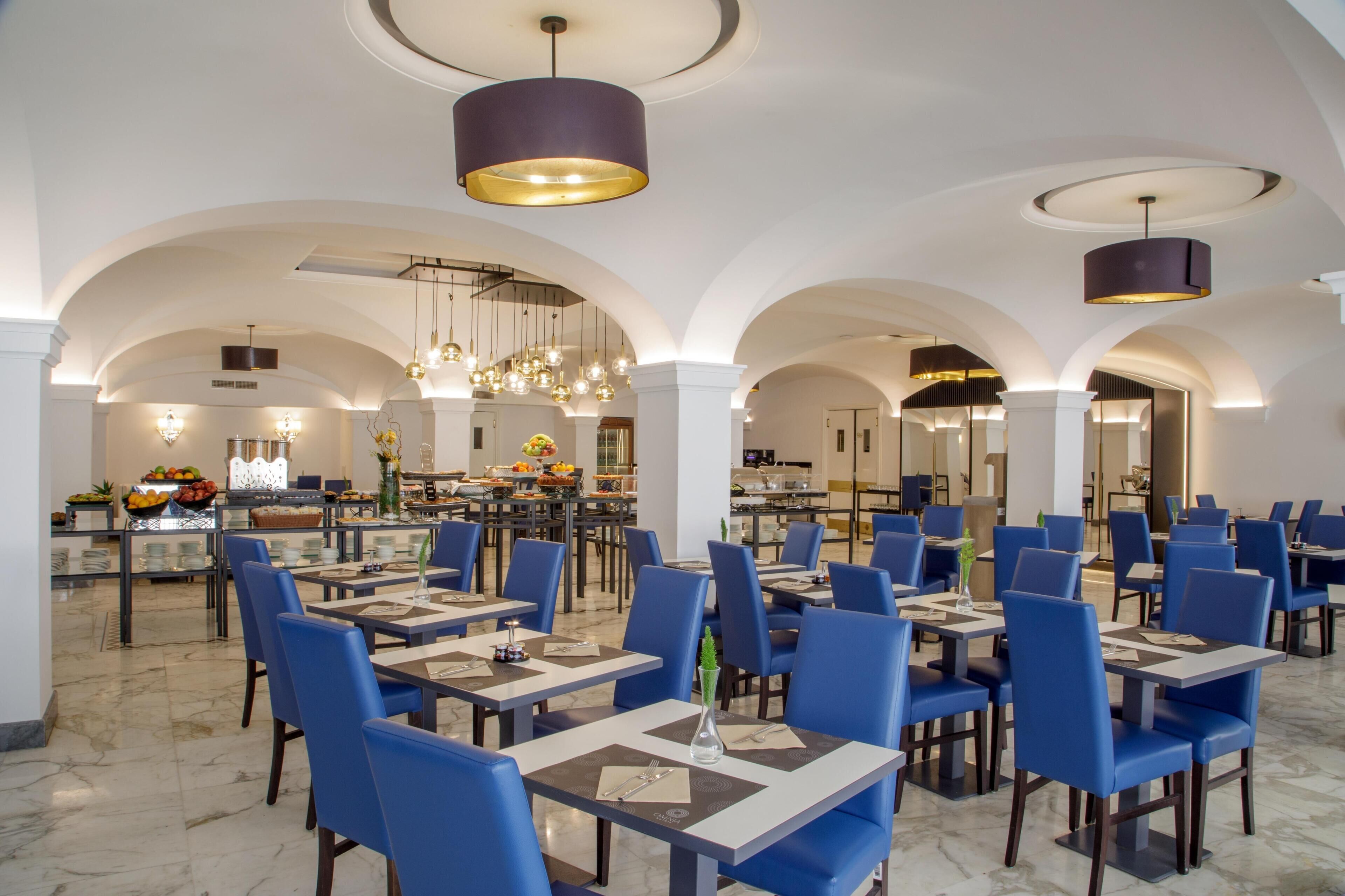 Un restaurant avec des chaises bleues, un sol en marbre et des luminaires suspendus.
