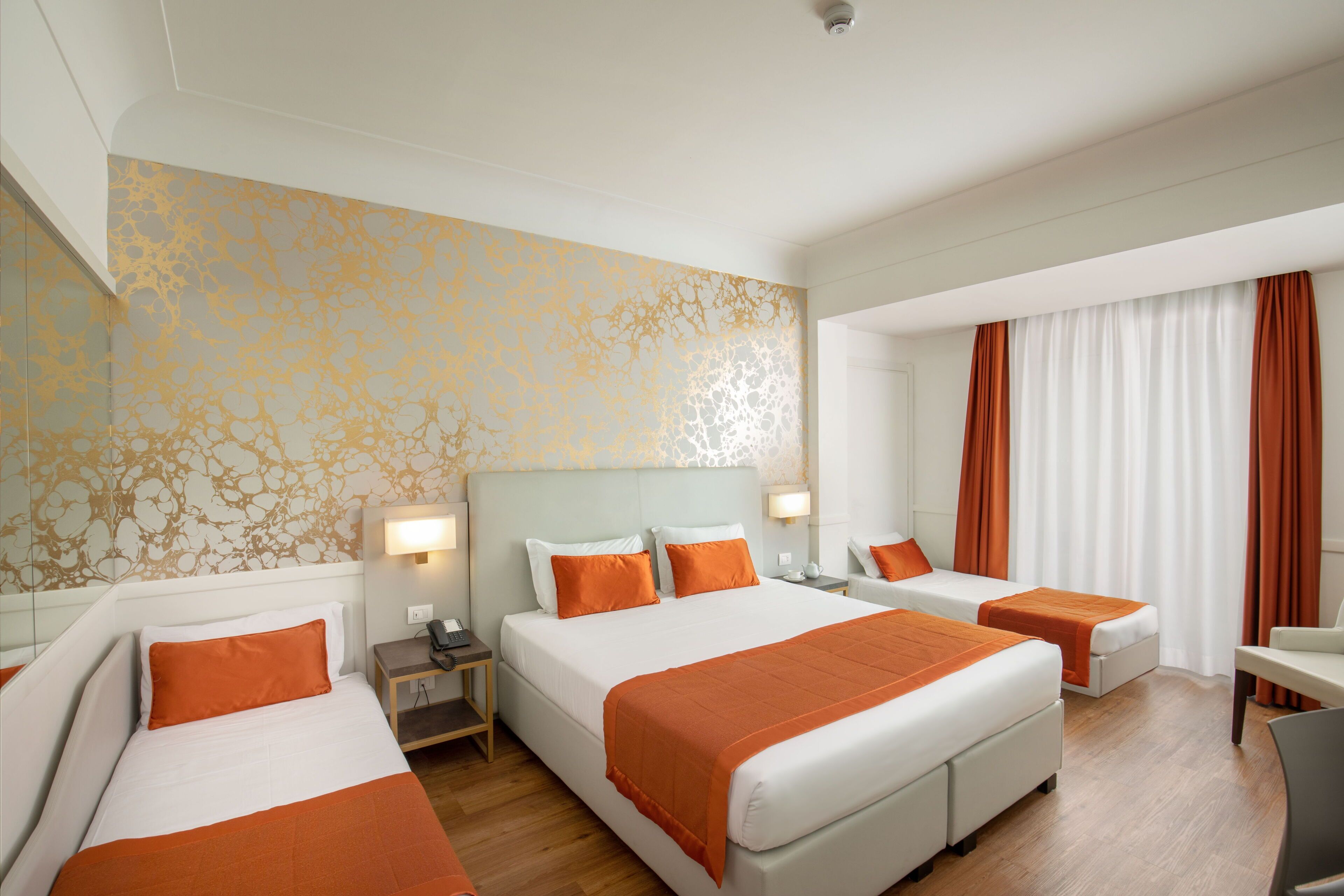 Ein Hotelzimmer mit einem großen Bett, zwei Einzelbetten, einem Schreibtisch und einem Sessel.