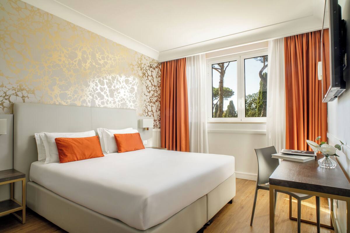 Una habitación de hotel con cama, escritorio y ventana con cortinas.
