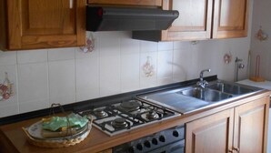 A kitchen with wooden cabinets, a gas stove, a sink, and a dishwasher. - "L'Antica Locanda" House (Catona)