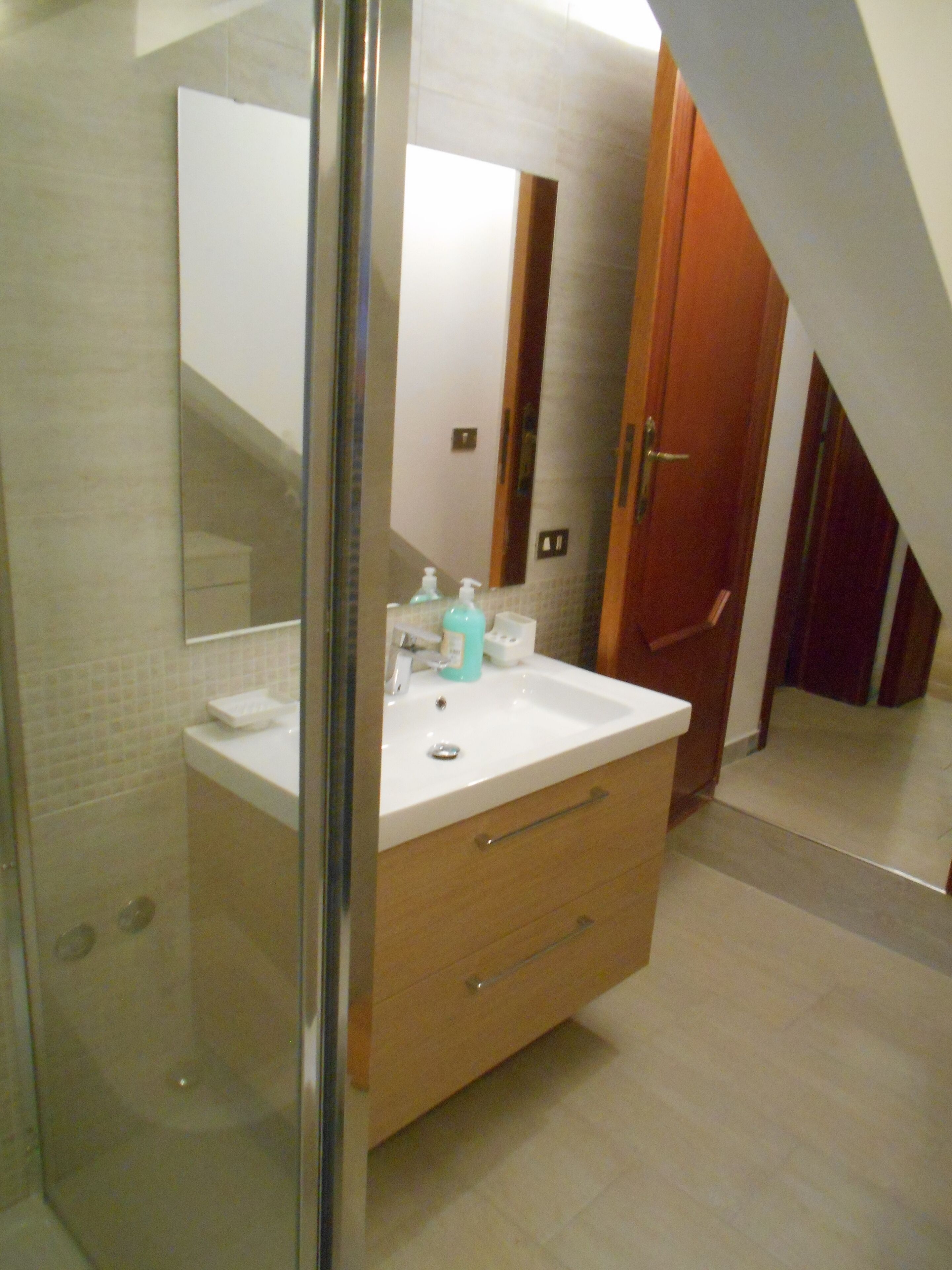 Une salle de bain avec une douche à parois de verre, un lavabo blanc avec un miroir au-dessus, et un meuble-lavabo en bois doté de tiroirs.