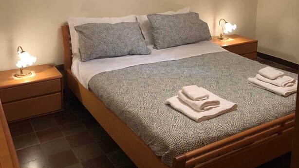 A neatly made bed with a patterned bedspread, two pillows, and folded towels on the side. There are two bedside tables with lamps, and a modern chandelier above the bed. - "L'Antica Locanda" House (Catona)
