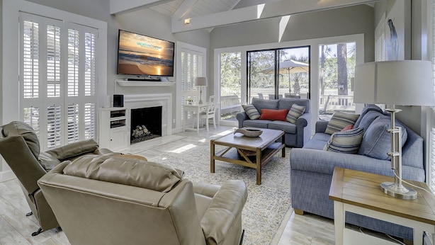 A spacious living room with a fireplace, a television mounted above it, and large windows offering a view of the outdoors. - 29 Stoney Creek - Harbour Town is just a quick walk away - Dog Friendly (Hilton Head Island)
