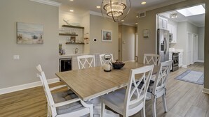 A dining area with a wooden table and white chairs, a chandelier, and kitchen cabinets in the background. - 29 Stoney Creek - Harbour Town is just a quick walk away - Dog Friendly (Hilton Head Island)