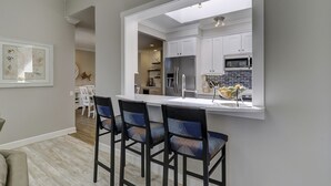 A modern kitchen with white cabinets, a stainless steel refrigerator, and a microwave. There are three bar stools with patterned cushions. - 29 Stoney Creek - Harbour Town is just a quick walk away - Dog Friendly (Hilton Head Island)