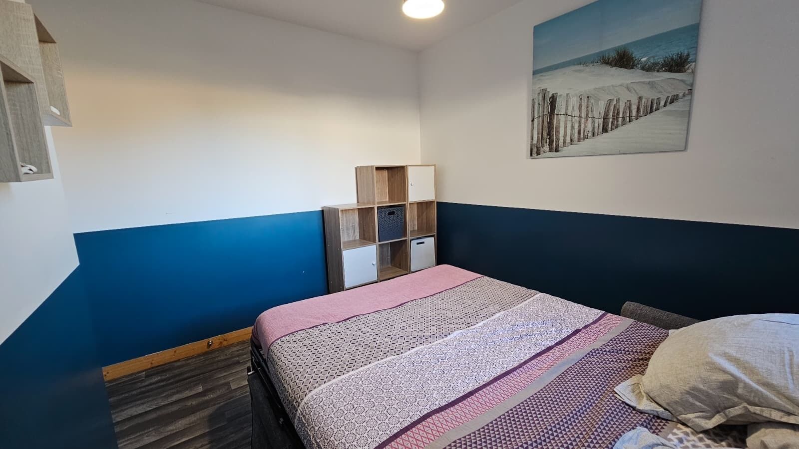 Une chambre à coucher avec un lit, une armoire en bois et un tableau accroché au mur.