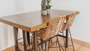 A dining area with a wooden table and woven chairs, a cactus plant, and decorative wall art. - Casita at base of the Superstition Mountains. Unbelievable hiking and views. (Apache Junction)