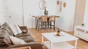 A living room with a brown leather sofa, a white coffee table, and a dining area with wicker chairs. - Casita at base of the Superstition Mountains. Unbelievable hiking and views. (Apache Junction)