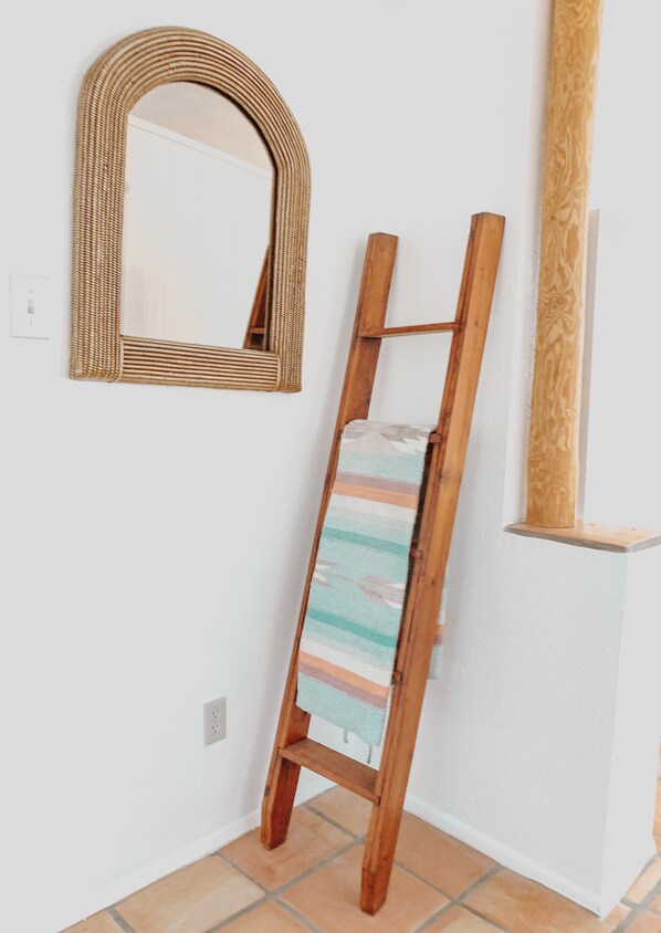 A wooden ladder leaning against a white wall with a woven mirror above it.