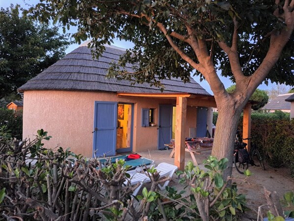 Ein kleines Haus mit einem Strohdach, einer blauen Tür und einem überdachten Vorbereich.