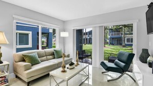 A modern living room with a sofa, a coffee table, and a chair. There is a large window and a door leading to an outdoor area. - 340A - Boca Retreat w/ Pool, Parking, Near Evert Tennis & Shops (Boca Raton)