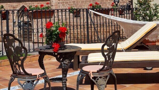 An outdoor patio with a table and chairs, a hammock, and a brick building with a bell tower in the background. - Palacio Azcarate Hotel (Ezcaray)
