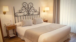 A neatly made bed with a decorative headboard, two bedside tables with lamps, and a wooden floor. - Palacio Azcarate Hotel (Ezcaray)