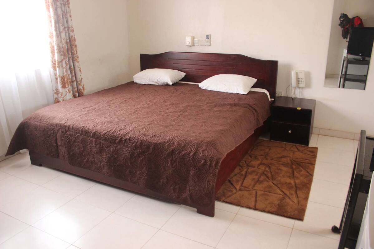 A bedroom with a large bed, two bedside tables, a nightstand, a mirror, and a telephone.