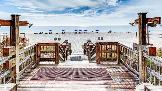 A wooden boardwalk leading to a beach with umbrellas and boats.