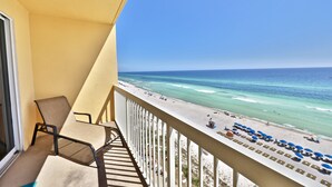 A balcony with a view of the beach, a chair, and a railing.