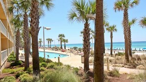 A pool area with palm trees, a beach, and a clear view of the ocean.