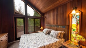 A bedroom with a large bed, wooden walls, a stained glass window, and a nightstand with a lamp. - Four Seasons (Yosemite)