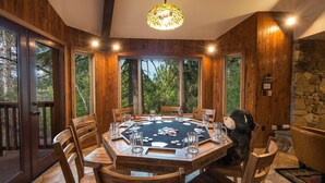A wooden-paneled room with a round table set for a game, large windows, and a stone wall. - Four Seasons (Yosemite)