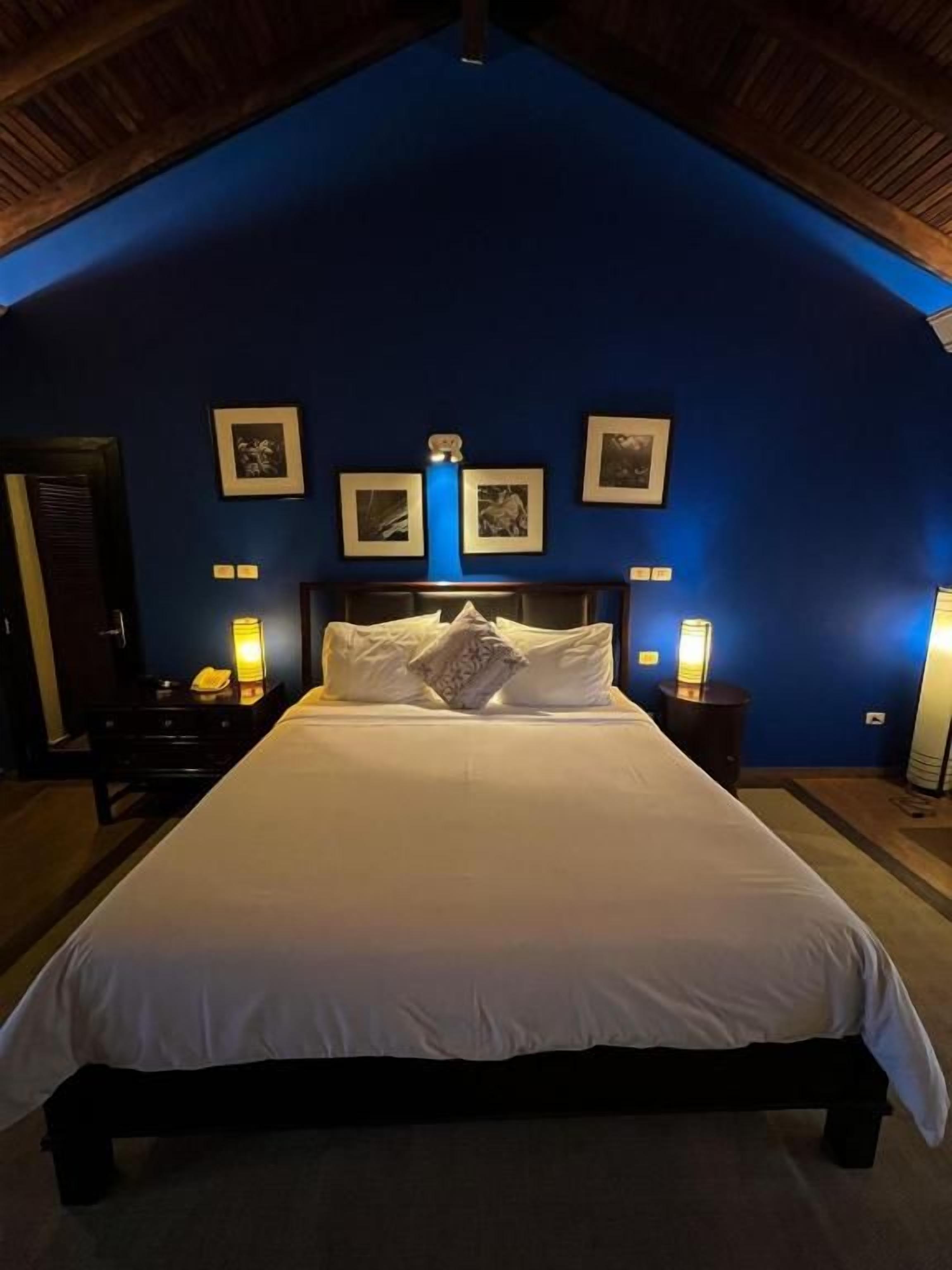 A bedroom with a large bed, a wooden ceiling, and framed pictures on the wall.