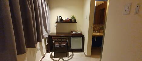 A compact kitchen with a refrigerator, a sink, and a small countertop. There is a chair and a table with a kettle and a basket on it.