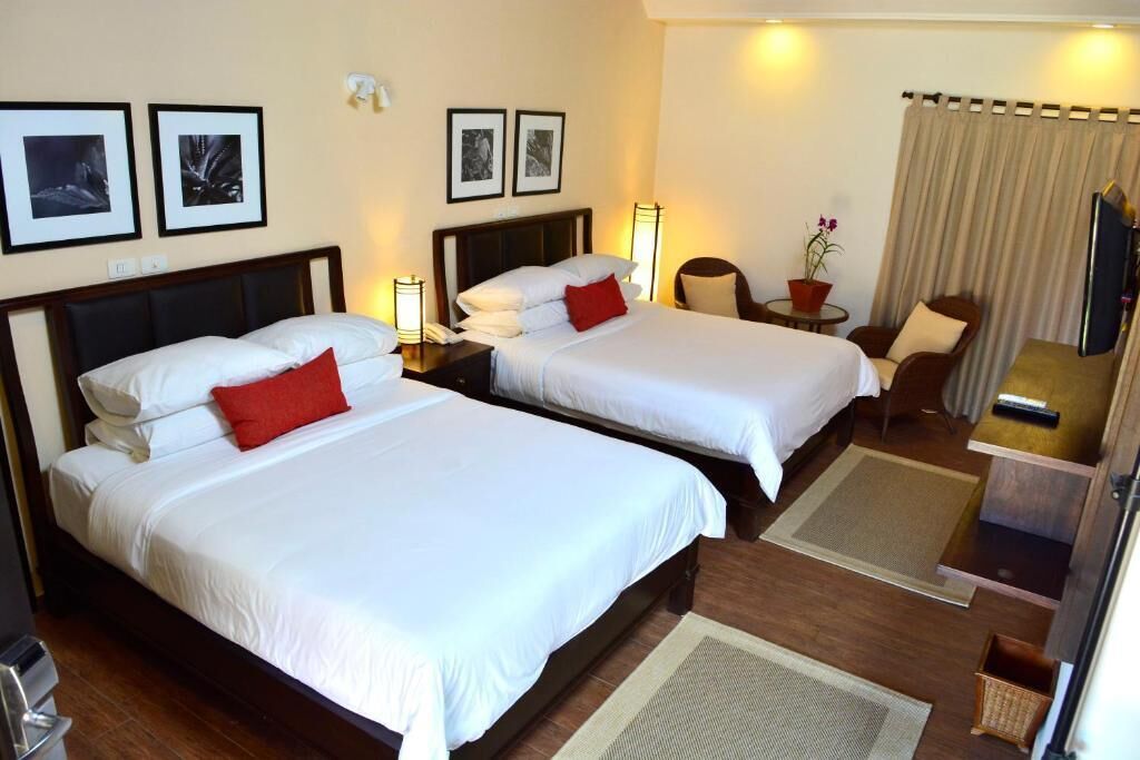 A hotel room with two beds, a desk, a chair, a TV, and framed pictures on the wall.