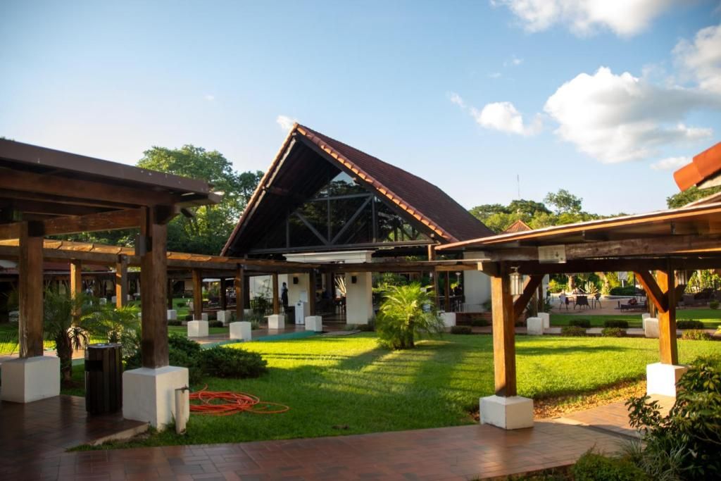 An outdoor covered area with a central building, surrounded by greenery and a paved walkway.