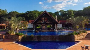 A swimming pool with a pavilion, surrounded by palm trees and a brick deck. - Alta Gracia Parque Hotel (Caacupé)