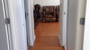 A hallway with wooden flooring leading to a living room with a patterned sofa.