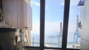 A compact kitchen with a view of a port and cranes, a refrigerator, and a sink.