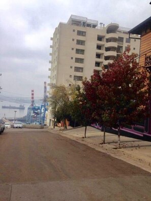 Un edificio a più piani con una facciata piatta, un'area di parcheggio antistante e un albero con foglie rosse alla destra.