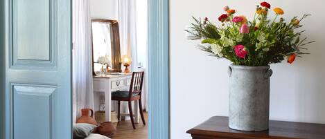 Ein Zimmer mit Schreibtisch aus Holz, Stuhl und einem Blumenstrauß auf einer Kommode.
