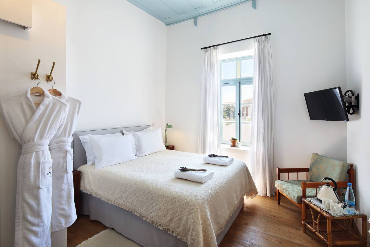 A bedroom with a bed, a TV, a chair, and a window with curtains.