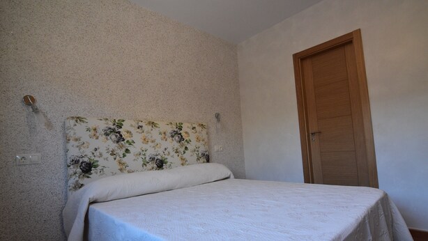 A bedroom with a floral-patterned headboard, a bed with a white bedspread, and a wooden door. - Self catering Tradición Rural for 8 people (Nieva)