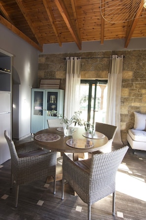 Cozy dining area with a round table and four chairs, surrounded by a stone wall and wooden ceiling with exposed beams.