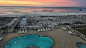 Un espace piscine offrant une vue sur la plage et l’océan au coucher du soleil.