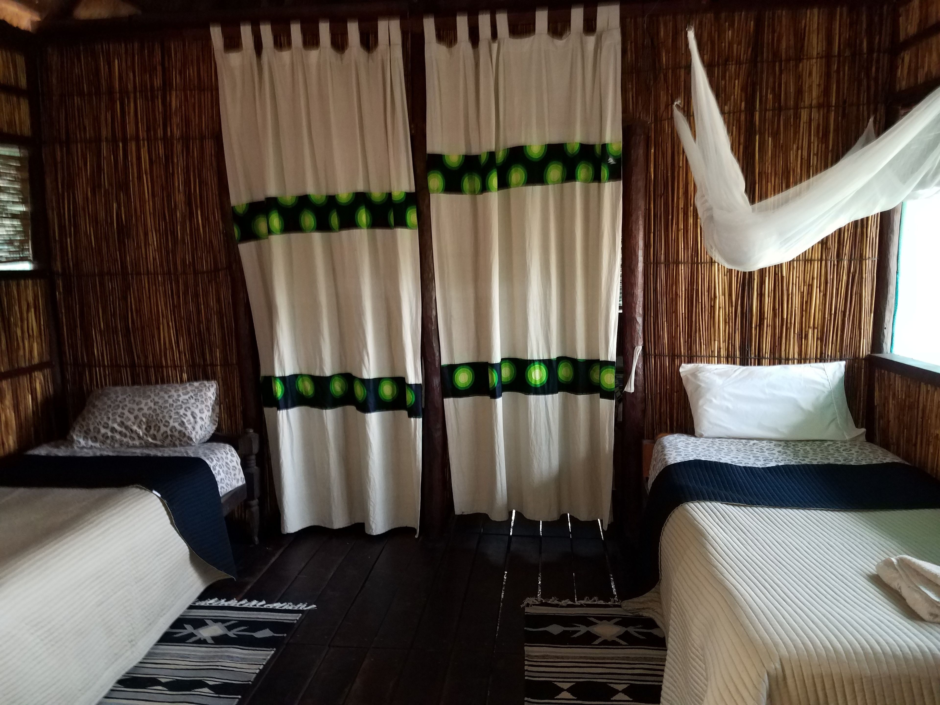 A room with two beds, a woven wall, and a curtain with green circles.