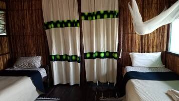 A room with two beds, a woven wall, and a curtain with green circles.
