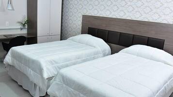 A hotel room with two single beds, a desk with a chair, and a small plant.