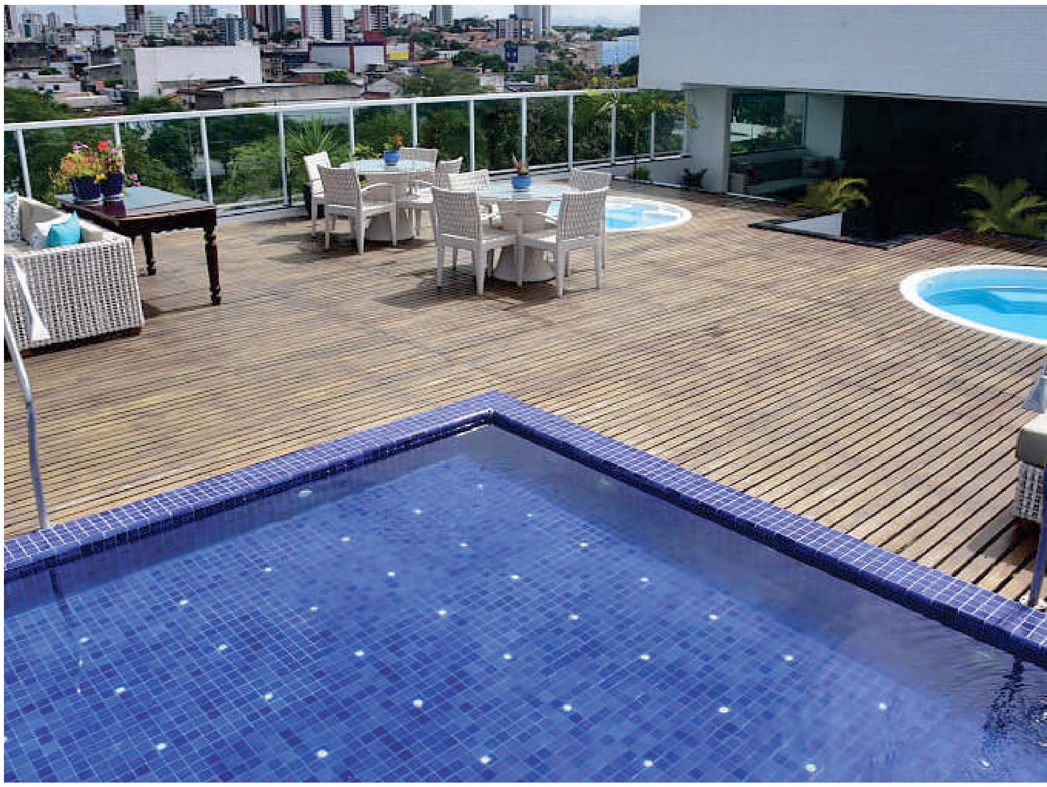 A rooftop pool area with a tiled pool, white outdoor furniture, and a city view.