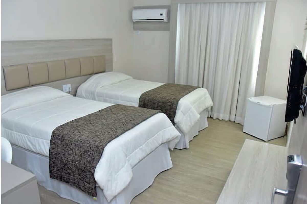 Une chambre d’hôtel avec deux lits, une télévision, une petite table et une fenêtre avec des rideaux.