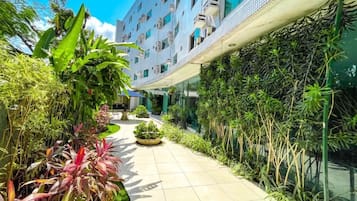 A modern building with a covered walkway, surrounded by lush greenery and potted plants.