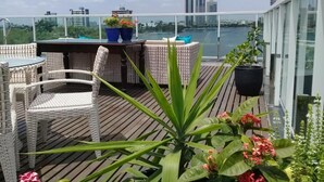 Een terras op het dak met rieten meubels, plantenpotten en uitzicht op de skyline van de stad.
