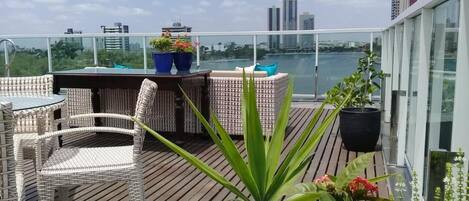 Terraço no telhado com mobiliário de vime, plantas em vasos e vista para o horizonte da cidade.