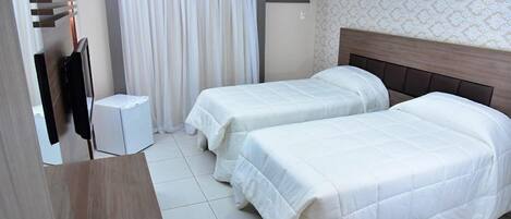Habitación de hotel con dos camas, televisión, una mesita y una cortina.