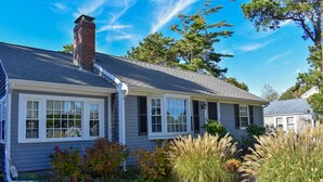 A single-story house with a grey siding exterior, a brick chimney, and a gravel driveway. - Two bedroom home located less than 2/10's of a mile to shared/private beach (Dennis Port)