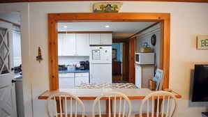 A kitchen with white cabinets, a wooden table, and three white chairs. - Two bedroom home located less than 2/10's of a mile to shared/private beach (Dennis Port)